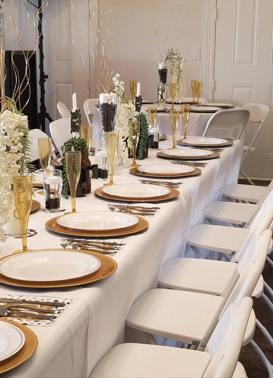 Long white and gold 50th birthday banquet table with gold chargers, taper candles and white berry centerpieces